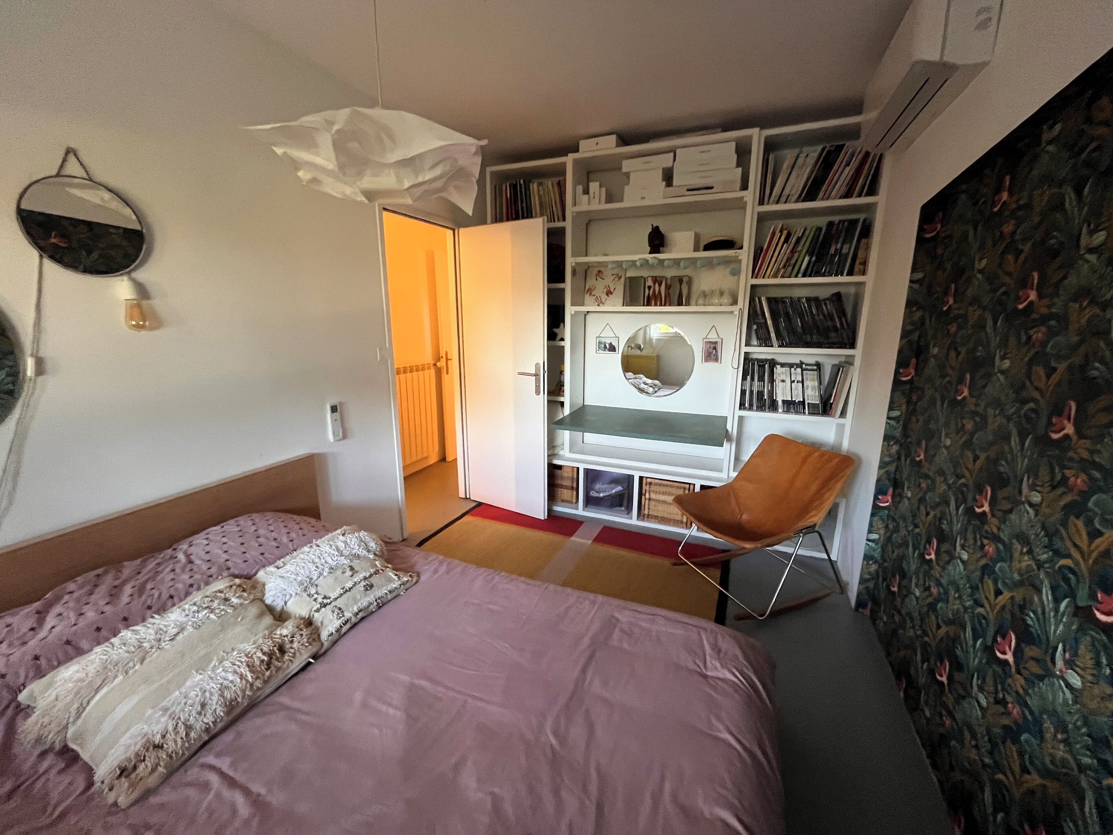 A bedroom with a bed, a chair, a bookshelf, and a mirror.