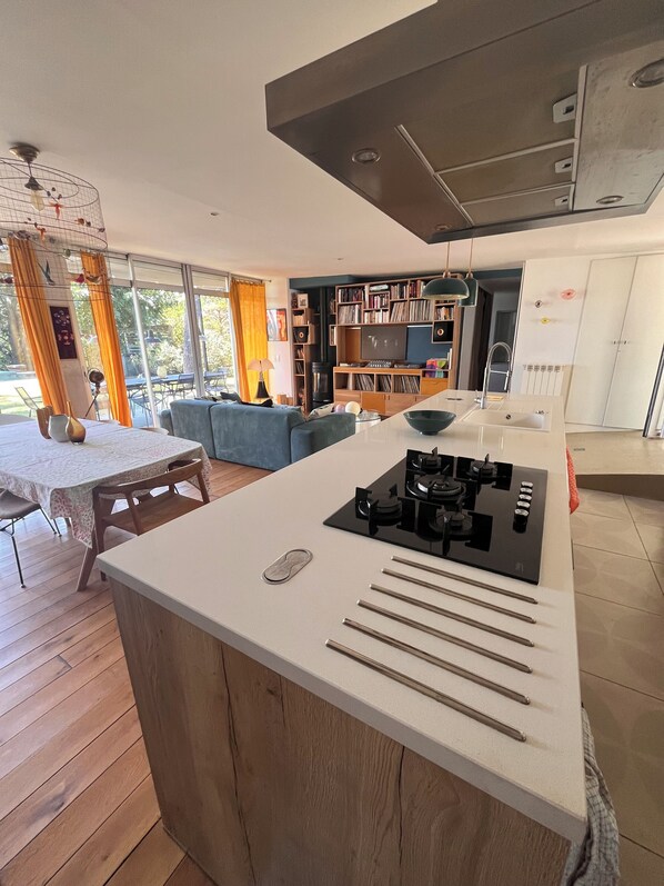 Une cuisine moderne dotée d’un îlot central, un coin repas avec une table et des chaises, et un salon avec un canapé et une bibliothèque.