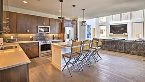 A modern kitchen with stainless steel appliances, a large island with bar stools, and a cozy living area with a large TV and sofa. - Peak Vistas | Walk to Trails | 4 Mins to Resort (Fraser)