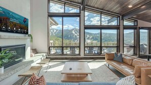 A spacious living room with large windows offering mountain views, a fireplace, and a modern interior design.