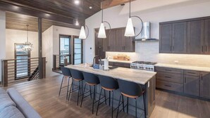 A modern kitchen with a central island, bar stools, dark cabinets, and pendant lighting.