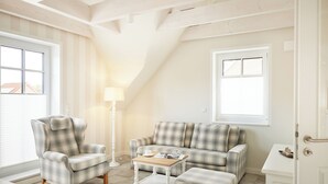 A cozy living room with a high ceiling, a plaid sofa, a matching armchair, a small coffee table, and a lamp.
