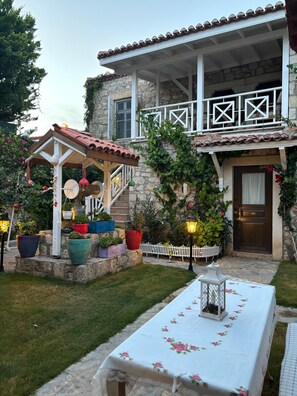 A stone building with a balcony, potted plants, and a table with a floral tablecloth. - Taşdelen Otel Alaçatı (Cesme)