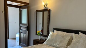 Een hotelkamer met een bed, een nachtkastje met een lamp, een spiegel en een deur naar een andere kamer.