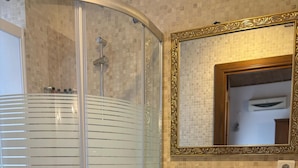 Een badkamer met een douche met glazen wand, een wastafel met kraan en een spiegel met een sierlijk frame.