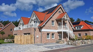 Ein zweistöckiges Haus mit rotem Ziegeldach, einem Balkon und einem Steinfundament.