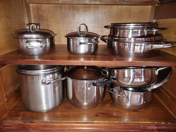 A wooden shelf with stainless steel cookware, including pots and pans.