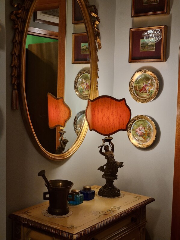 A vintage-style mirror with ornate frame, a table lamp, and decorative plates on a dresser.