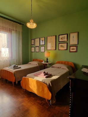 Une chambre avec deux lits, une table, une lampe et des tableaux encadrés accrochés au mur.