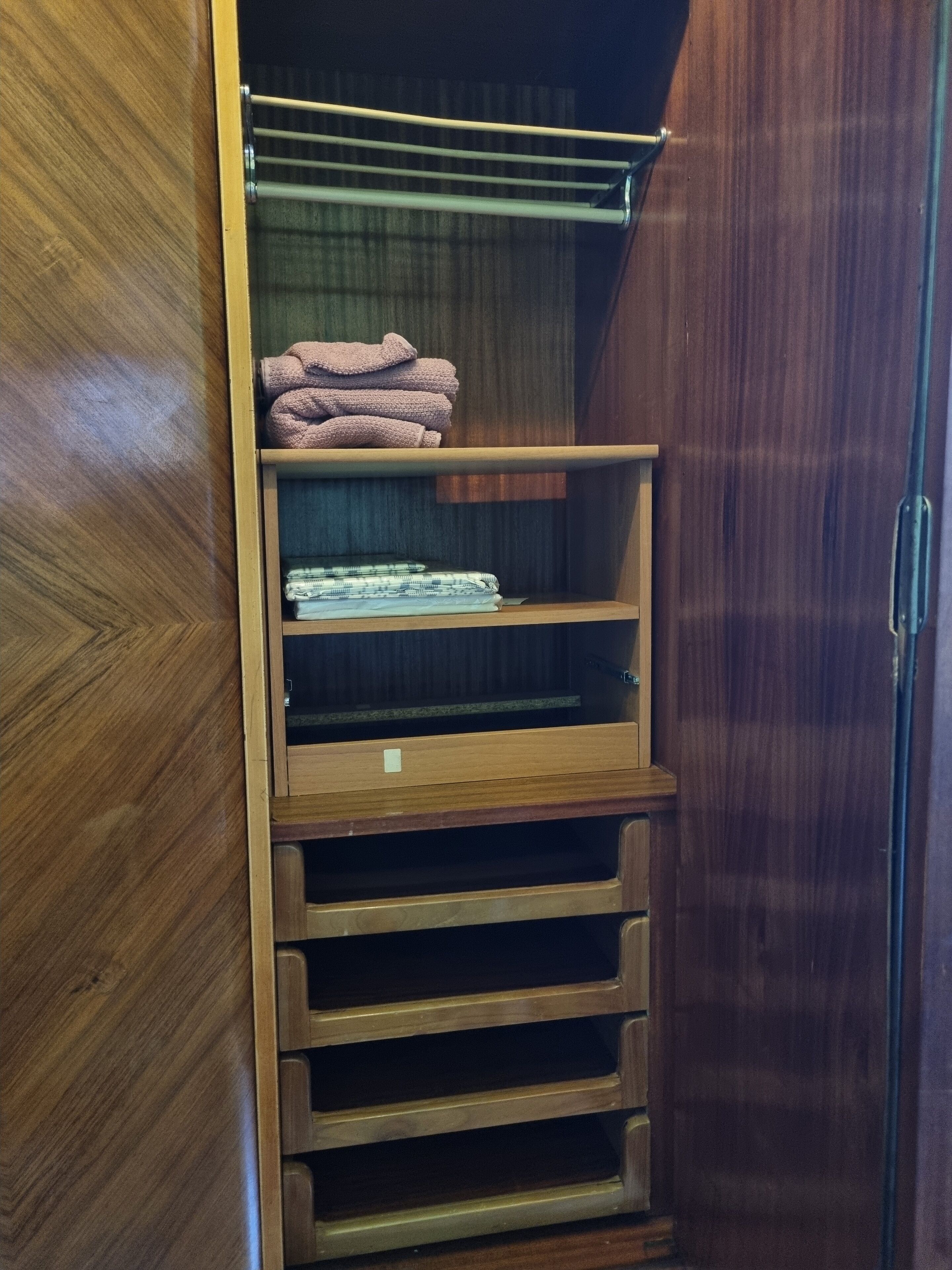 Een houten garderobe met meerdere planken en lades, met daarin opgevouwen handdoeken en een opgevouwen kledingstuk.