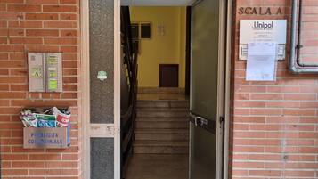 Ein Gebäudeeingang mit Backsteinfassade, einer Metalttür, einer Treppe, die nach innen führt, und einem Schild mit 'Unipol' auf der rechten Seite.
