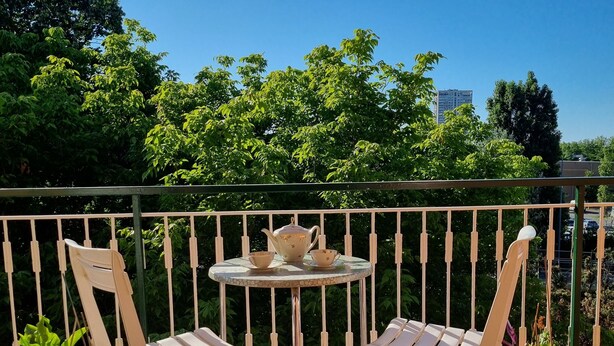 Un balcon avec deux fauteuils blancs, une petite table ronde avec une théière et des tasses, et des plantes en pot.