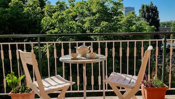 Een balkon met twee witte lounge stoelen, een klein rond tafeltje met een theepot en kopjes, en potplanten.