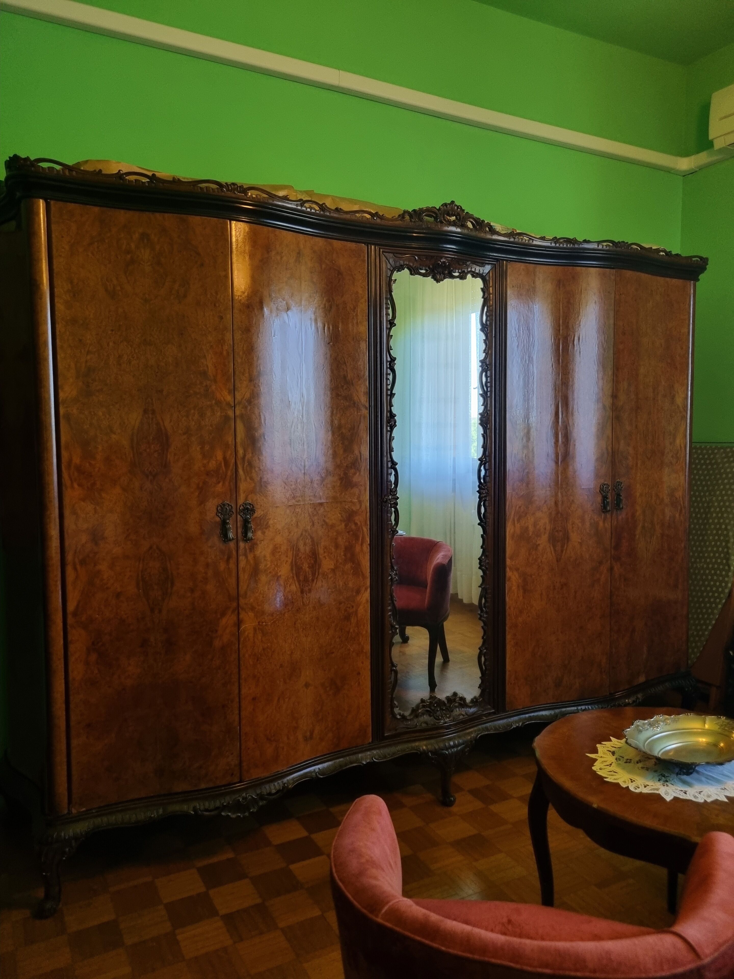 A room with a large wooden wardrobe, a red chair, and a round table with a placemat.