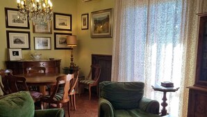 Un salon traditionnel avec des meubles recouverts d’un tissu vert, un lustre, des tableaux encadrés aux murs et un coin repas comprenant une table et des chaises en bois.