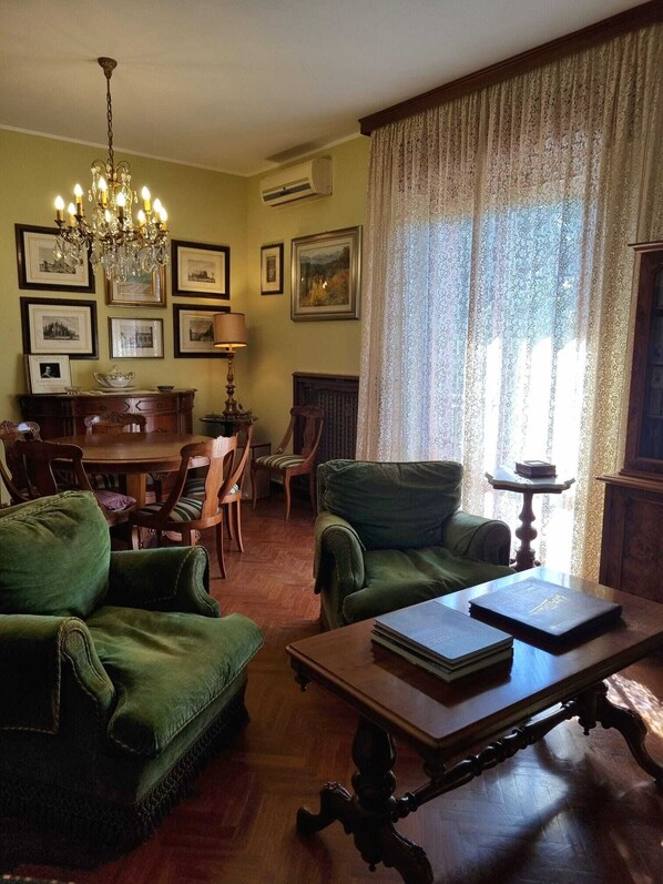 A traditional living room with green upholstered furniture, a chandelier, framed pictures on the walls, and a dining area with a wooden table and chairs. - 950mt sea, 500mt center, apartment 120sqm 3rd floor elevator 5 beds 3 rooms (Rimini)