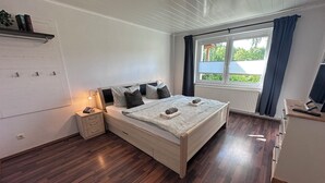 A bedroom with a bed, bedside table, lamp, and a window with curtains. - Modern Holiday Home with Garden and nature near Warnow (Warnow)