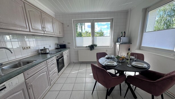A modern kitchen with white cabinetry, a dining table set for four, and a window providing natural light. - Modern Holiday Home with Garden and nature near Warnow (Warnow)