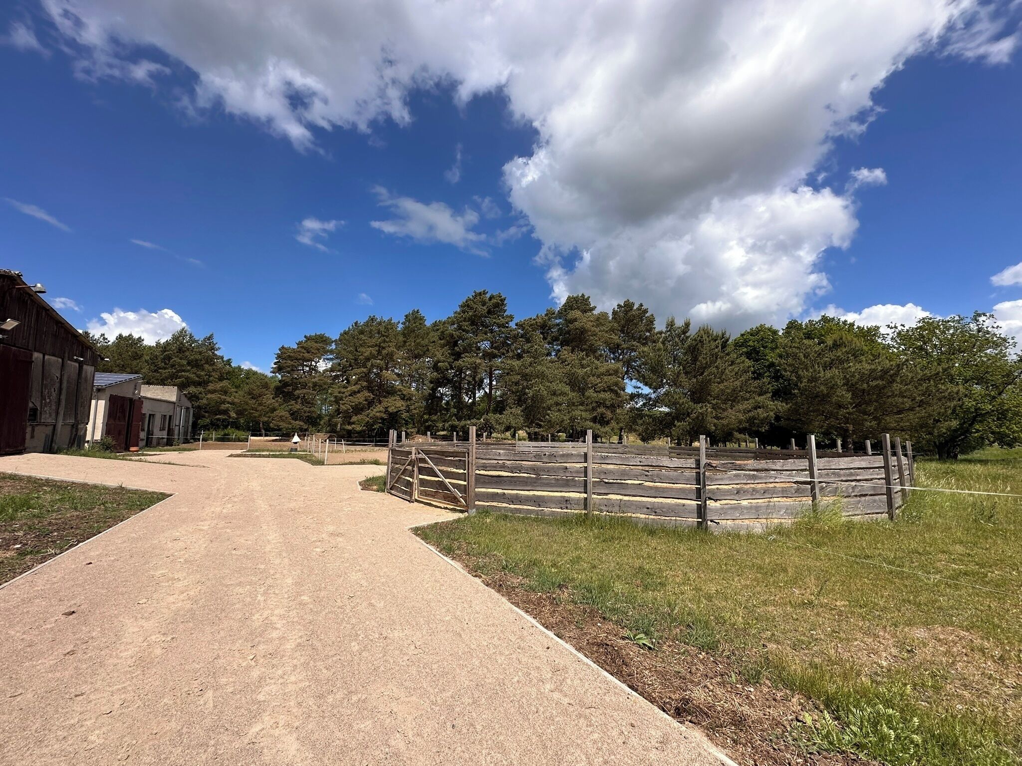 A rural property with a dirt path leading to a fenced area, surrounded by trees and a barn.