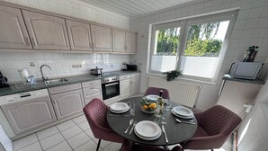 A modern kitchen with white cabinets, a dining table set for four, and a window with blinds. - Modern Holiday Home with Garden and nature near Warnow (Warnow)