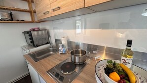 A modern kitchen with wooden cabinets, a stainless steel sink, a built-in stove, and a bowl of fruit on the counter.