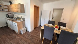 A compact kitchen with modern appliances, a dining area with a table and chairs, and a small trash bin.