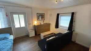 A compact room with a bed, a small bedside table, a dresser, a bench, and a window with blinds.
