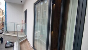 Un balcón residencial con puerta de cristal, un pequeño espacio para sentarse al aire libre y vista a la calle.