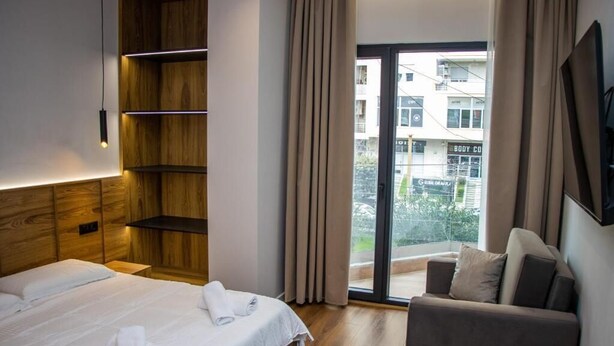 Una habitación de hotel con una cama, una estantería de madera, un sofá y un balcón con vistas a la ciudad.