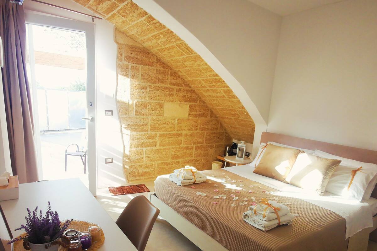 A bedroom with a bed, a table with a plant and candles, and a stone wall.
