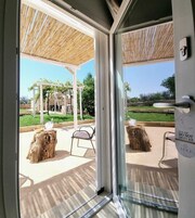 Puerta de vidrio que da a un patio exterior con una pérgola, dos taburetes de madera y un cartel de 'No molestar'.