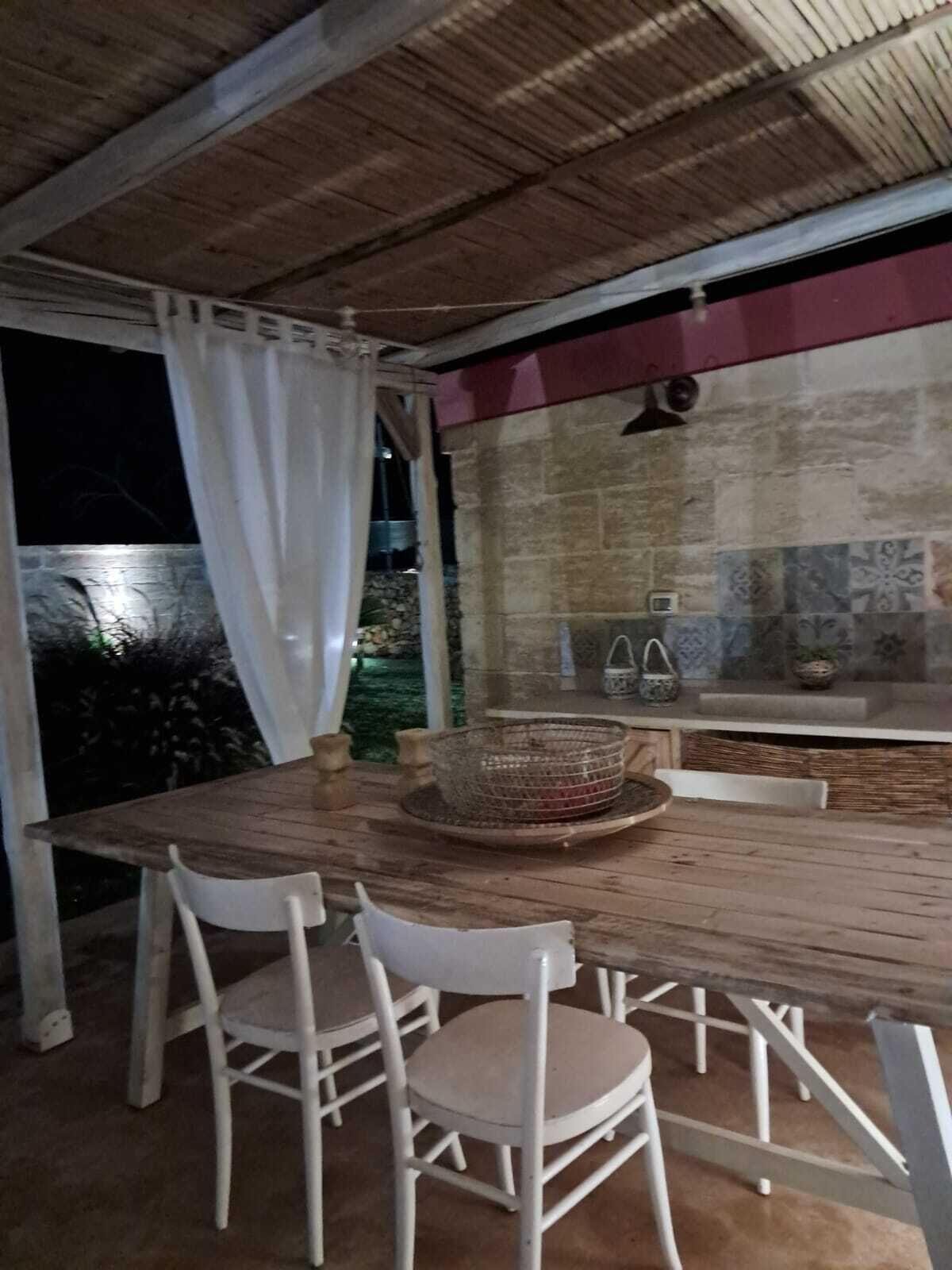 Een buiten eethoek met een houten tafel en witte stoelen, een mand en een betegelde achterwand.