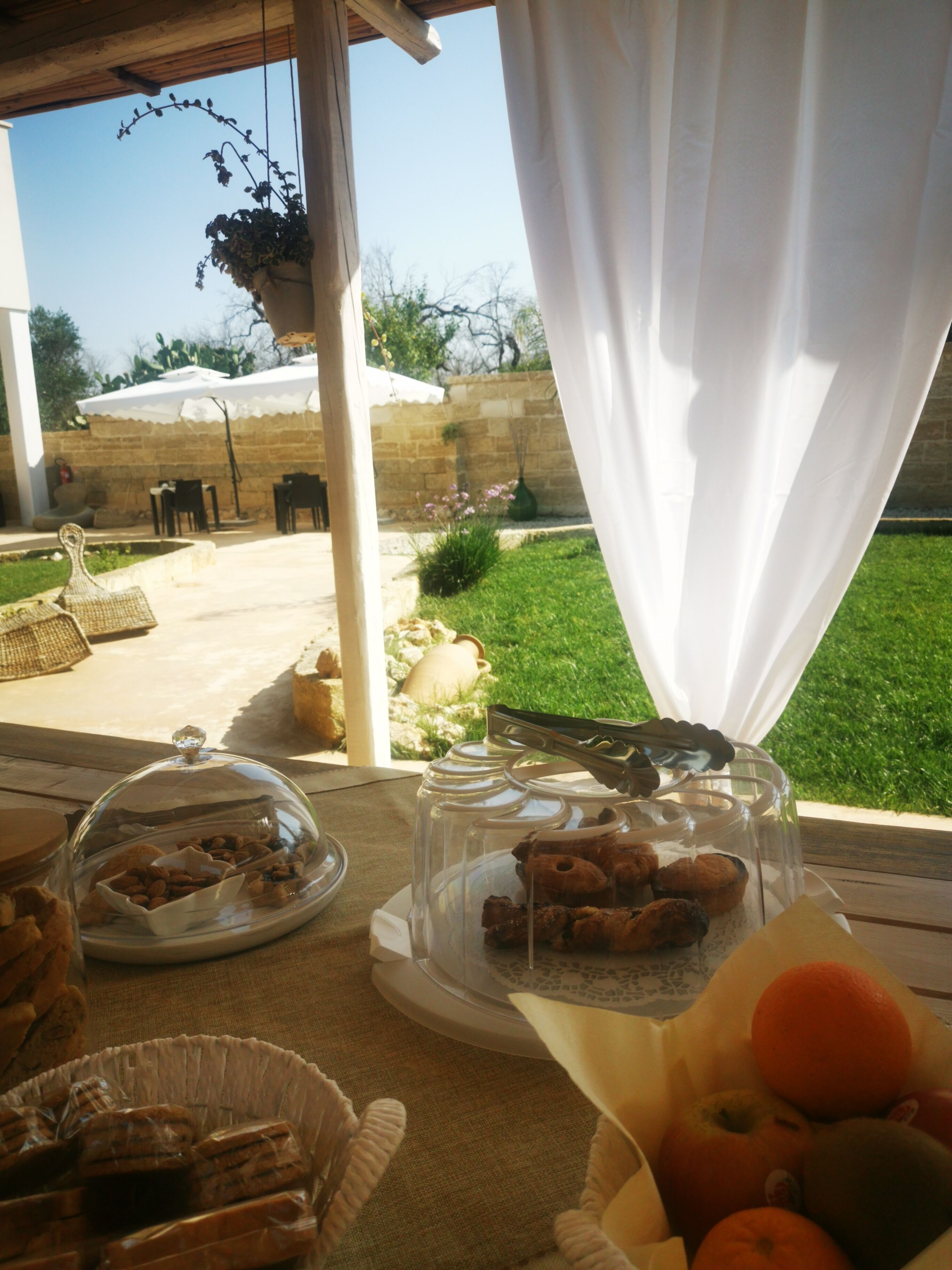 Un espace de restauration en plein air avec une table dressée pour le petit-déjeuner, comprenant du pain, des viennoiseries et des fruits.