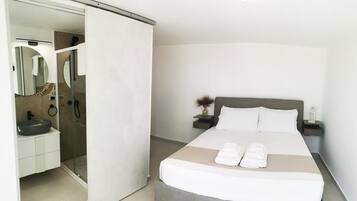 Un dormitorio moderno con cama, mesitas de noche, baño con lavabo y espejo, y una puerta corrediza a la zona de ducha.