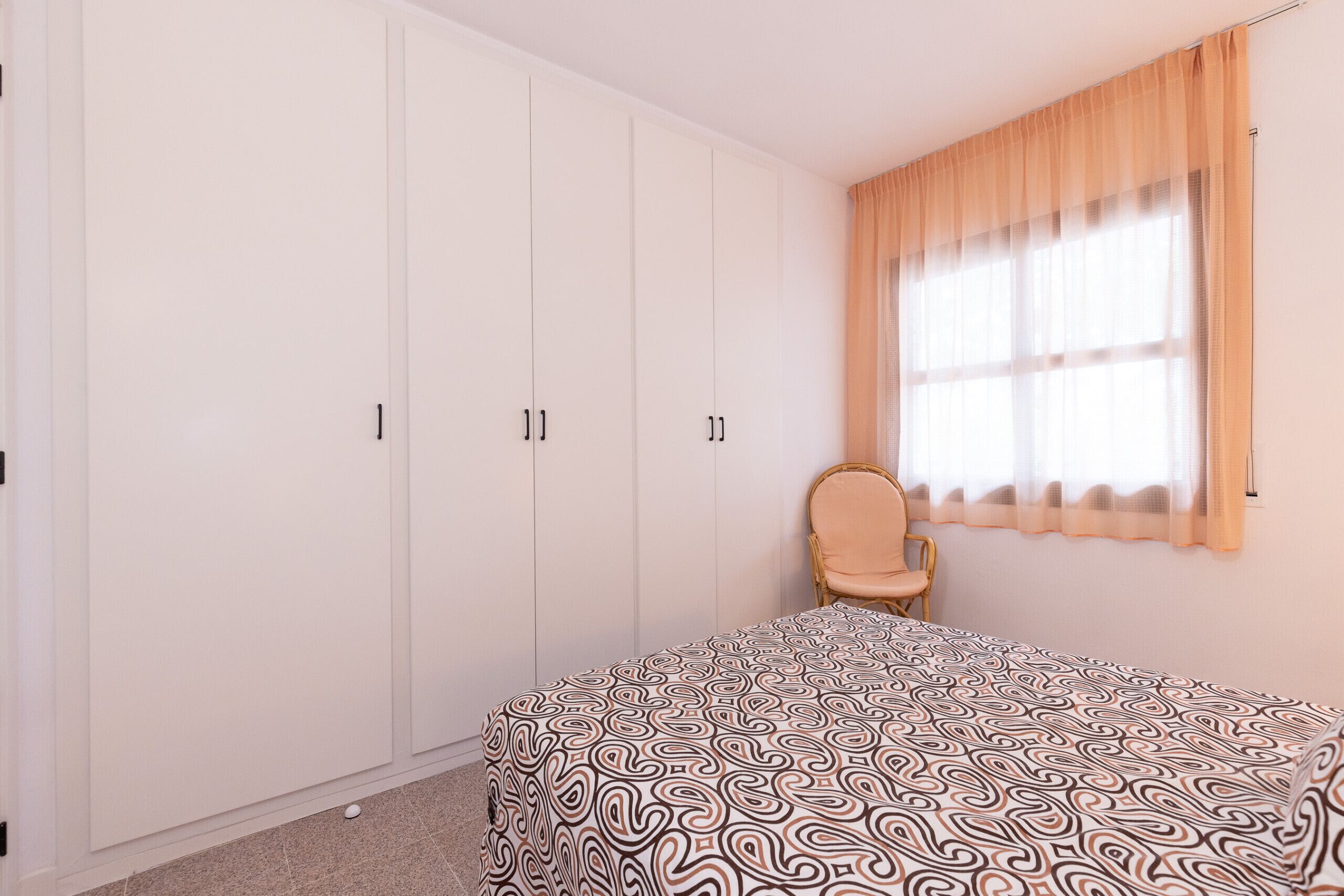 A bedroom with a bed, a wardrobe, a chair, and a window with curtains.