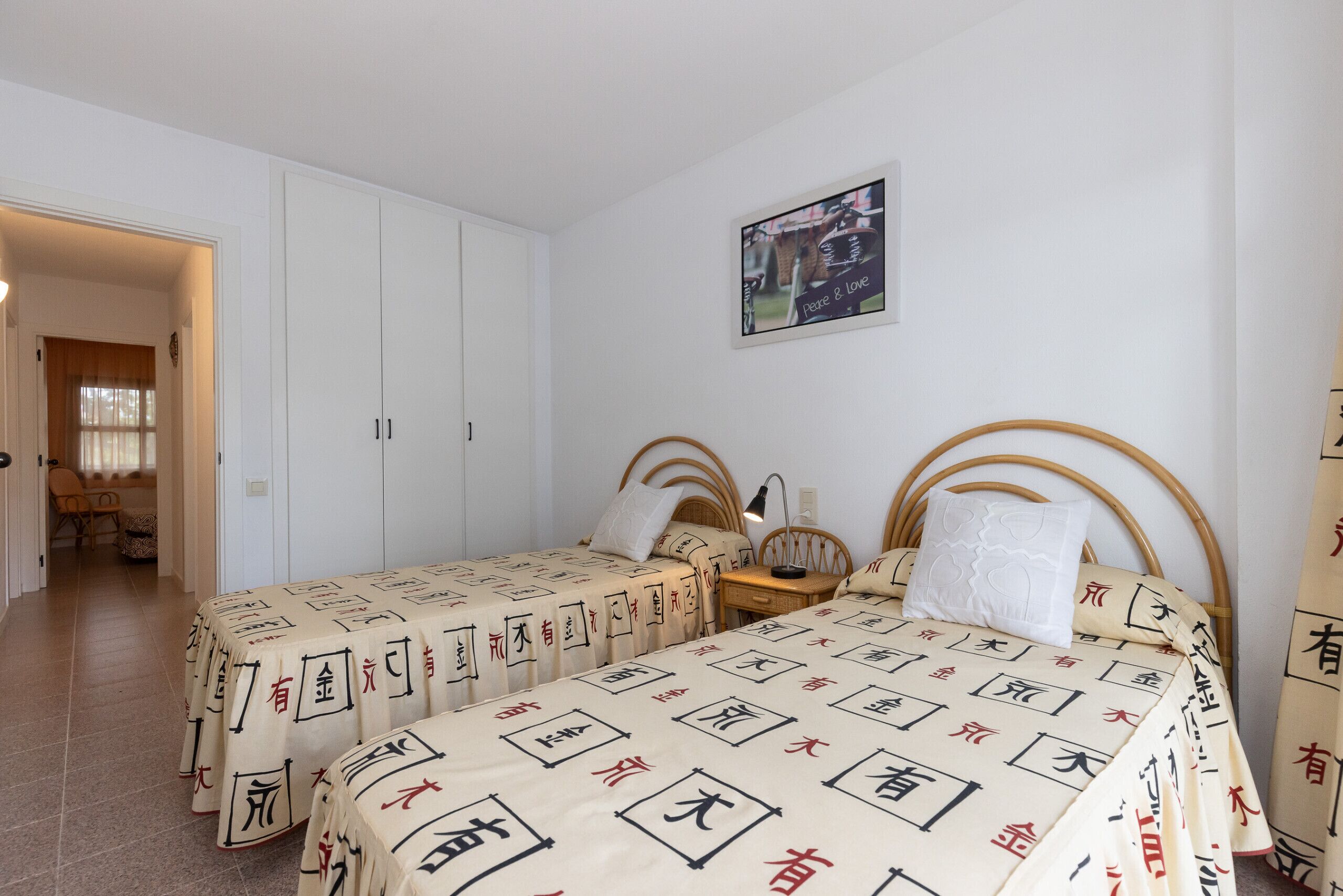 Ein Schlafzimmer mit zwei Betten, einem hölzernen Kopfende, einem Nachttisch und einem an der Wand hängenden Bild.