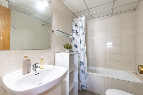 Une salle de bain avec un lavabo blanc, un miroir, un rideau de douche à motifs bleus et une baignoire.