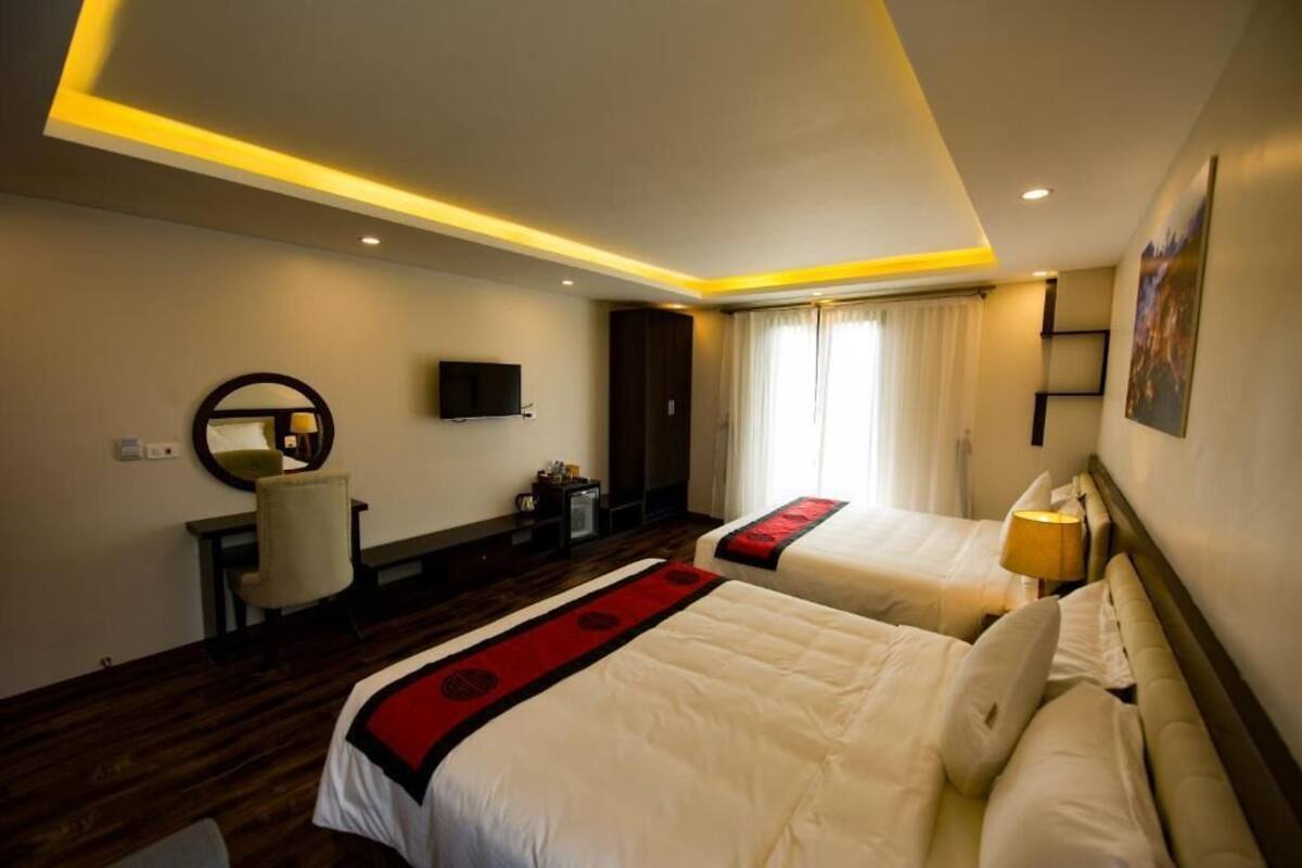 Een hotelkamer met twee bedden, een bureau, een stoel, een televisie en een raam met gordijnen.