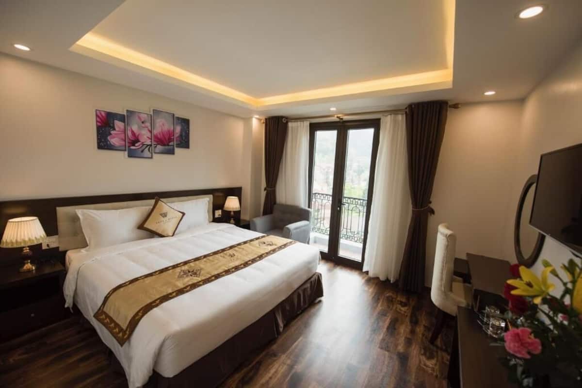 Een hotelkamer met een groot bed, een bureau met stoel, een televisie en een balkon met gordijnen.