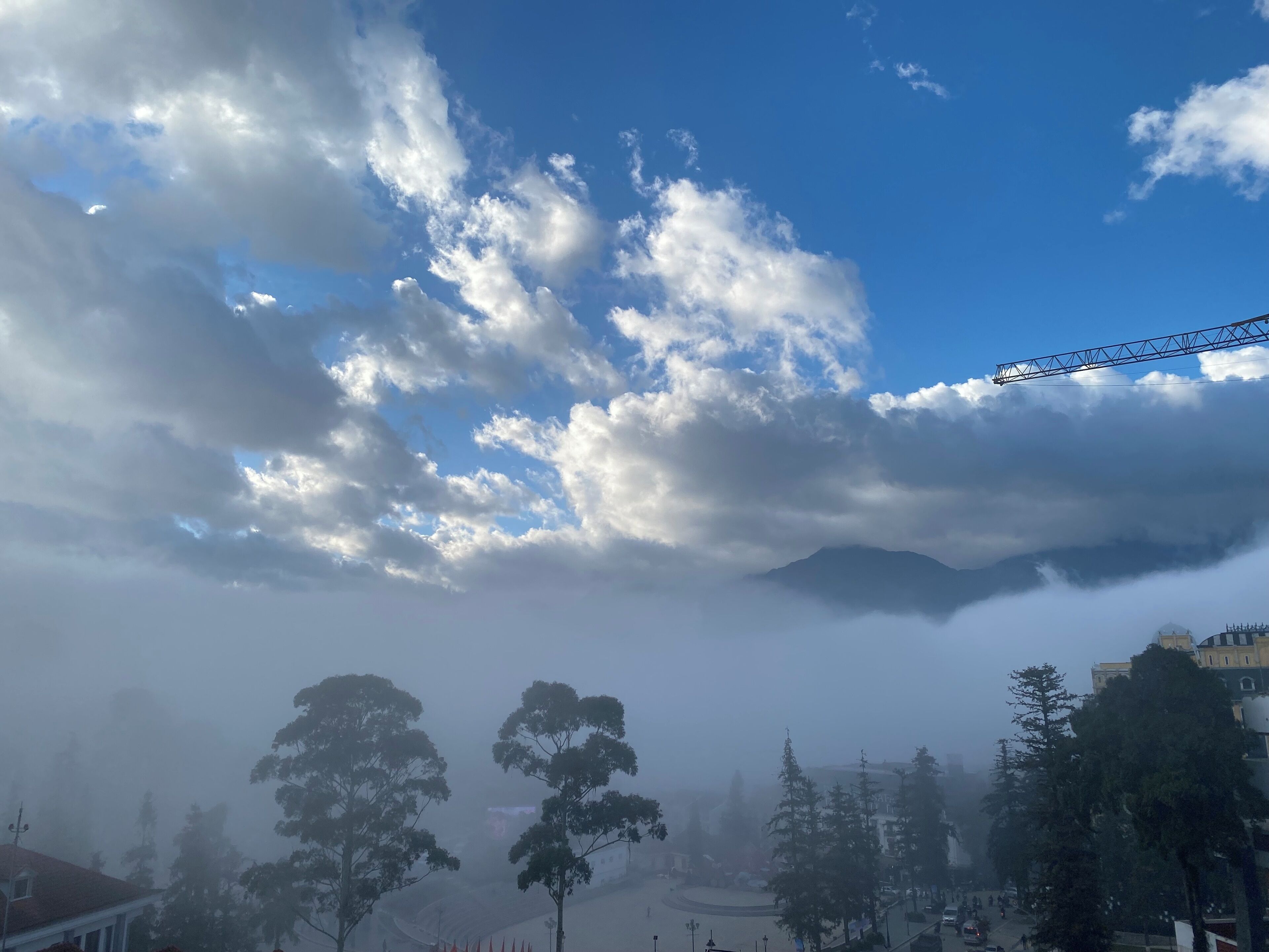 A view of a town with a mountain in the background, trees, and a clear sky with clouds.