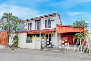 Una casa de dos pisos con techo rojo, paredes blancas y un patio delantero cercado.