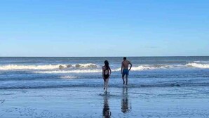 Uma cena de praia com duas pessoas caminhando em direção ao oceano.