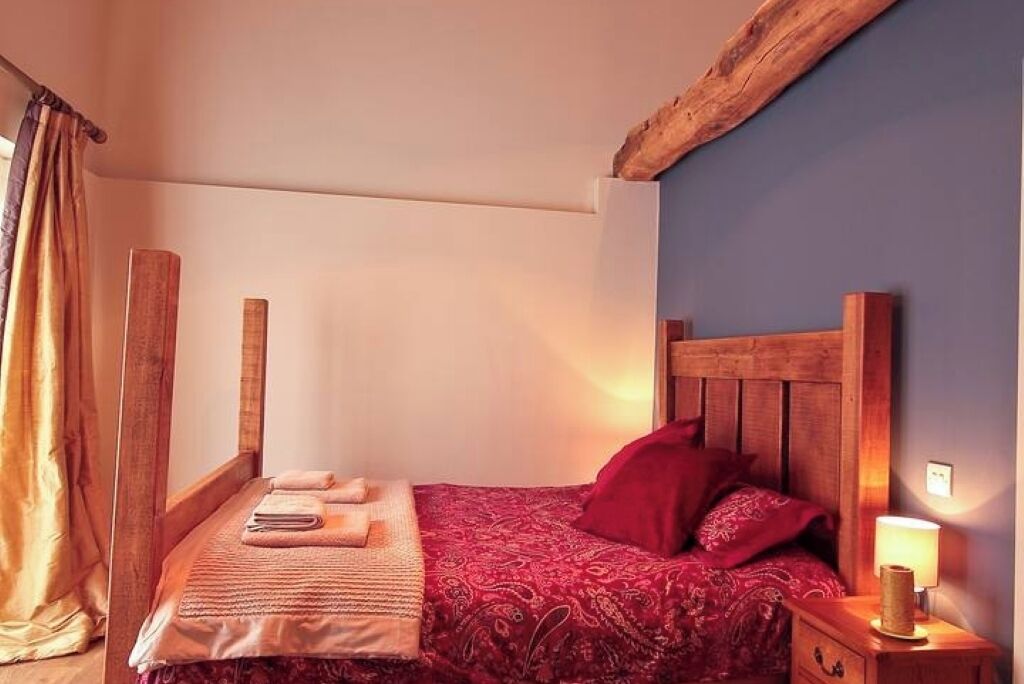 A cozy bedroom with a wooden headboard, a red patterned bedspread, and a bedside lamp.