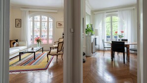 A spacious living room with a large window, a sofa, a coffee table, and a dining area with chairs and a table.