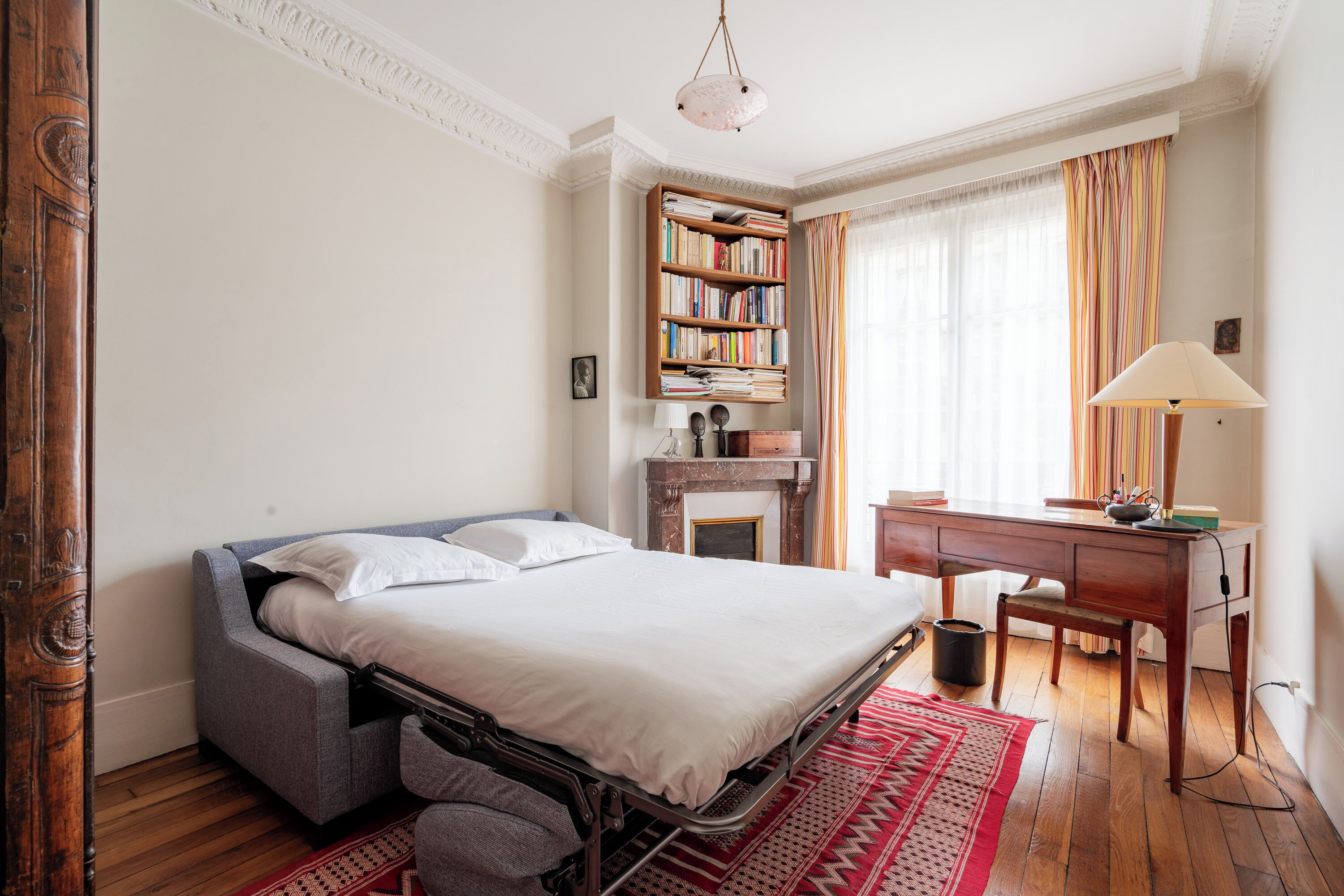 A bedroom with a bed, a desk, a bookshelf, and a fireplace.