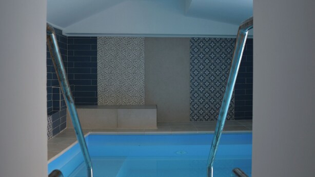A view of a swimming pool from a poolside area with a tiled wall and a metal ladder. - Luxurious retreat for your well-being (Valle dell'Angelo)
