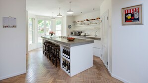 Une cuisine moderne dotée d’un îlot central, de tabourets de bar, de bouteilles de vin et offrant une vue sur l’extérieur.