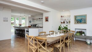 Un vaste espace dédié à la salle à manger, avec une table et des chaises en bois, une cuisine à l’arrière-plan et un tableau accroché au mur.