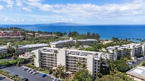 A high-rise hotel with multiple balconies, a parking lot, and a view of the ocean.