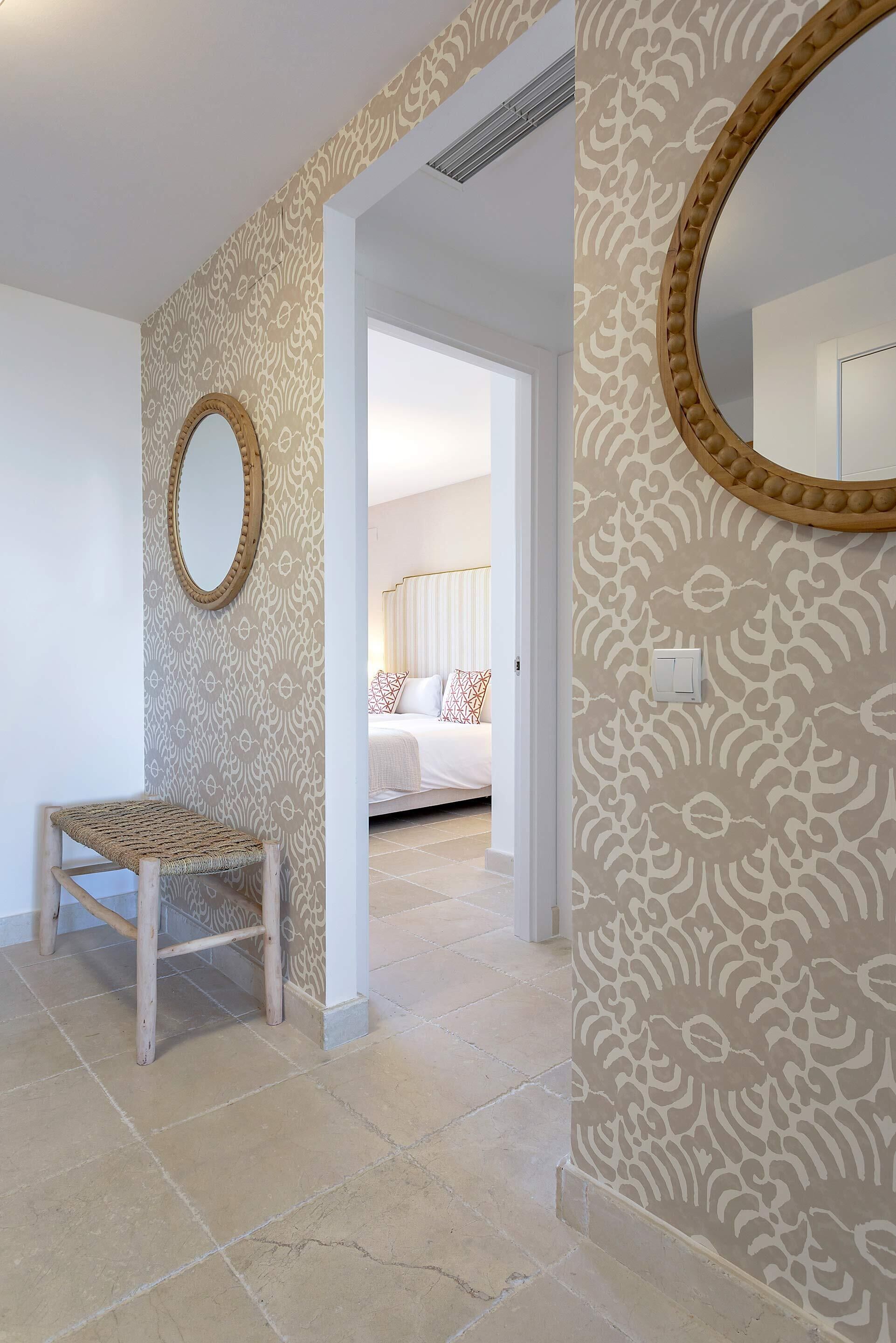 Ein Flur mit gemustertem Wandpapier, einer Holzbank und einem runden Spiegel an der Wand.